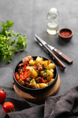 Patates, soğan ve biberli kızarmış domuz eti. Ulusal ev yapımı Gürcistan yemeği siyah bir tavada, arka planda taze domates, bitki ve gölgelerle birlikte. Metin için boş alan.