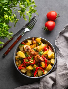 Patates, soğan ve biberli kızarmış domuz eti. Ulusal ev yapımı Gürcü yemeği Ojakhuri koyu arka planda bir kasede taze domates ve bitkiyle birlikte. Üst görünüm.
