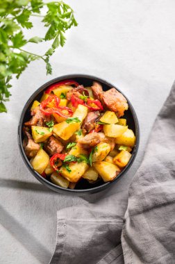 Patates, soğan ve biberli kızarmış domuz eti. Ulusal ev yapımı Gürcistan yemeği siyah bir kase içinde taze bitki, peçete ve gölgelerle birlikte. Üst görünüm 