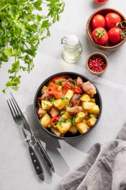 Patates, soğan ve biberli kızarmış domuz eti. Ulusal ev yapımı Gürcistan yemeği siyah bir kase içinde taze bitki, domates ve baharatlı. Üst görünüm 