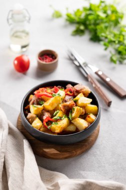 Patates, soğan ve biberli kızarmış domuz eti. Ulusal ev yapımı Gürcistan yemeği siyah bir kasede taze bitki ve domatesli hafif bir arka planda.. 