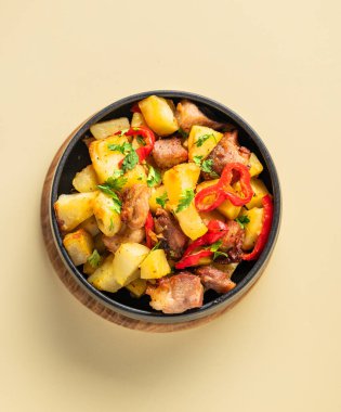 Patates, soğan ve biberli kızarmış domuz eti. Ulusal ev yapımı Gürcistan yemeği sarı arka planda siyah bir kase içinde. Üst görünüm.