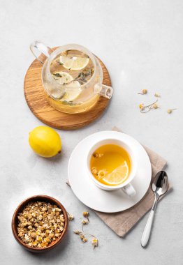 Beyaz bardakta limonlu papatya çayı ve arka planda çiçekli çaydanlık. Sağlık ve uyku için sağlıklı bir detoks içeceği konsepti. Üst görünüm. 