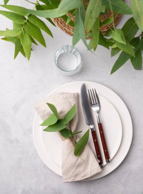 Okaliptüs dallı hafif bir arka planda kutlama için iki beyaz tabak ve camla şenlik masası. Restoran menüsü konsepti. Üst görünüm.