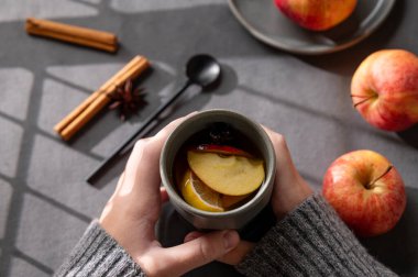 Ellerinde ev yapımı elma kokteyli ya da arkaplanda taze meyve ve baharatlı elma ve tarçınlı gri bir bardak var. Sonbahar ya da kış sağIıklı içecek kavramı. Üst görünüm.