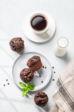 Hafif arka planda naneli bir tabakta çikolatalı kekler bir fincan kahve, süt ve peçeteyle. Kahvaltıda pişirilen ev yapımı sağlıklı konsept. Üst görünüm.
