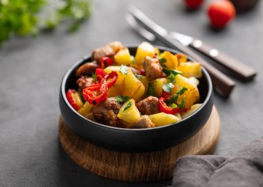 Patates, soğan ve biberli kızarmış domuz eti. Ulusal ev yapımı Gürcistan yemeği, siyah bir tavada, arka planda taze domates ve bitkilerle kaplanmış.. 