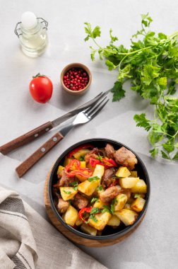 Patates, soğan ve biberli kızarmış domuz eti. Ulusal ev yapımı Gürcistan yemeği siyah bir kasede taze bitki, baharat ve domatesli. Üst görünüm.