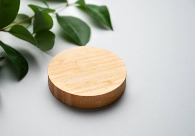 Modern boş ürün görüntüsü. Asgari ahşap, gri arka planda yeşil yapraklı podyum. Ürün sunumu, satış veya kozmetik reklam afişi için sahne konsepti. Boşluğu kopyala