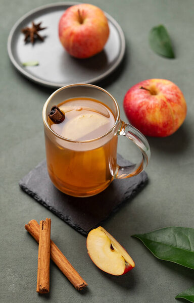 Homemade apple punch with fresh apples, cinnamon and spices in cup on a green background with fresh fruits and branch. A hot healthy autumn drink.