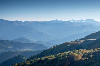 Yeşil ağaçlarla, mavi gökyüzüyle ve güneşli bir günde kar zirveleriyle güzel bir dağ manzarası. Gürcistan dağlarında seyahat etmek. Gomismta Köyü.