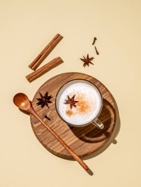 Geleneksel Hint masala chai latte 'si. Sütlü, baharatlı ve otlu sıcak içecek, sarı arka planda, sert gölgeli ahşap bir tahtada. Üst görünüm ve kopyalama alanı.