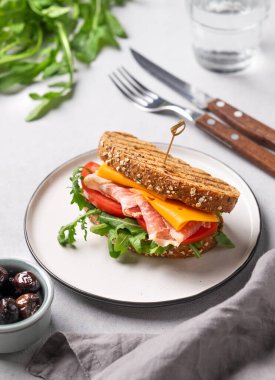 Çedar peynirli tahıl ekmeğinden yapılmış tost sandviçi domates ve roka ile doldurulmuş domuz pastırması zeytin ve bir bardak suyla hafif bir zemin üzerinde. Sağlıklı ve beslenme kahvaltısı kavramı. 