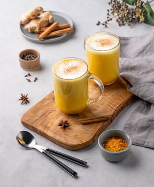 Baharatlı ve ballı zerdeçal altın sütlü latte. Detoks, bağışıklık arttırıcı, iltihap önleyici, sağlıklı, rahat bir içecek, tahta bir bardakta, arka planda hafif bir arka planda..