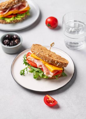 Çedar peynirli buğday ekmeğinden yapılmış iki tost kulübü sandviçi ve zeytinli domates, marul ve roka ile doldurulmuş domuz pastırması. Sağlıklı ve beslenme kahvaltısı kavramı.