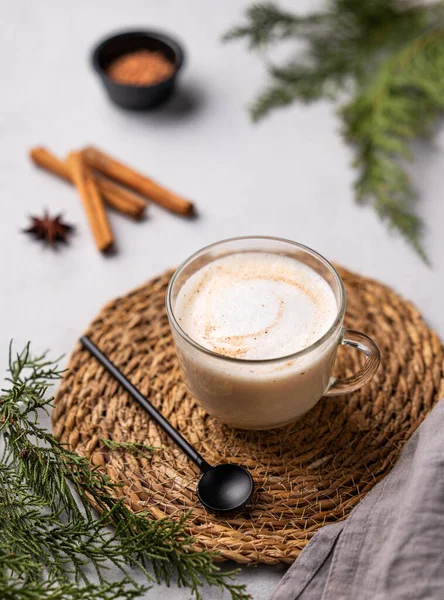 Spiced coffee latte or cappuccino with cinnamon sticks on a light background with fir branches. The concept of a Christmas warming drink. Festive winter mood.