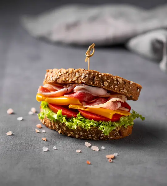 Club sandwich on a board with a bacon, cheese, tomato and lettuce on a dark background close up with napkin. The concept of a healthy snack for breakfast or lunch.