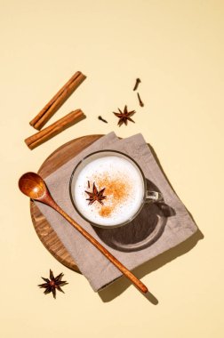 Geleneksel Hint masala chai latte 'si. Sütlü, baharatlı ve otlu sıcak içecek, sarı arka planda, sert gölgeli ahşap bir tahtada. Üst görünüm ve kopyalama alanı.