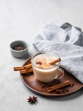 Geleneksel Hint masala chai latte 'si. Sütlü sıcak içecek, baharatlar ve otlar beyaz arka planda, siyah biber ve peçeteyle birlikte ahşap bir tabakta. Metin için boş alan.