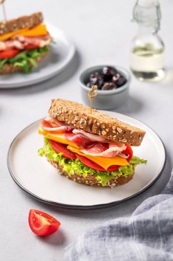 Çedar peynirli buğday ekmeğinden yapılmış tost kulübü sandviçi domates ve marulla doldurulmuş domuz pastırması zeytin ve yağlı hafif bir zemin. Sağlıklı ve beslenme kahvaltısı kavramı.