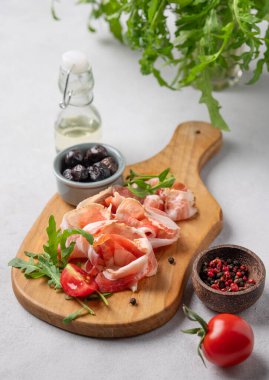 Hafif arka planda zeytin, baharat, domates ve bitkilerle birlikte domuz pastırmalı ya da jambonlu abur cubur tahtası. Antipasto kavramı. 