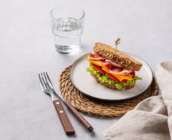Toast club sandwich made of grain bread with cheddar cheese and bacon stuffed with tomatoes and lettuce on a light background with glass of water. Healthy and dietary breakfast concept. 