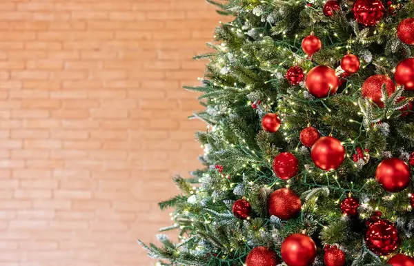 Christmas tree with red decorations and lights on a brick wall background. Holiday background concept for New Year card, banner or winter product advertisement. Free space for text.