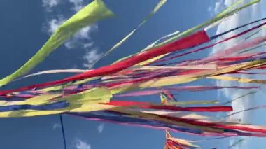 Çok renkli kurdeleler ya da çelenkler, güneşli bir yaz gününde bulutlu mavi gökyüzü ile rüzgarda sallanır. Dini törenler için şenlikli bir dekorasyon konsepti. Yoga festivaline geri çekilin..
