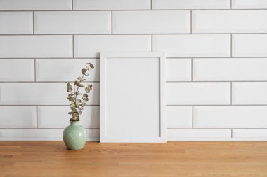 Beyaz kiremit bir duvara karşı boş bir tuval ve vazo ile ahşap bir masanın üstünde duran bir çerçeve. Fotoğraf, poster ya da resim tasarımı. Boşluğu kopyala.