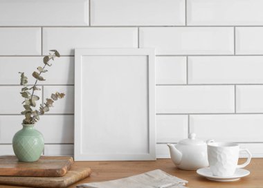 Beyaz kiremit bir duvara karşı boş bir tuval ve vazo ve bir fincan çayla ahşap bir masanın üstünde duran bir çerçeve. Fotoğraf, poster ya da resim tasarımı. Boşluğu kopyala.