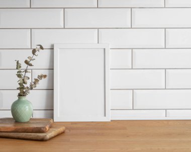 Beyaz kiremit bir duvara karşı boş bir tuval ve vazo ile ahşap bir masanın üstünde duran bir çerçeve. Fotoğraf, poster ya da resim tasarımı. Boşluğu kopyala.