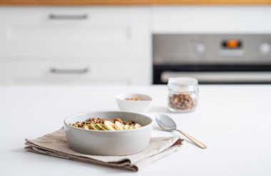 Beyaz mutfak arka planında muz ve kivi ile pişirilmiş granola. Sağlıklı kahvaltı konsepti: Vejetaryen yoğurt, müsli ve taze meyve. Boşluğu kopyala.