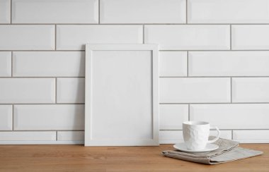 Beyaz kiremit bir duvara karşı boş bir tuval ve bir fincan çayla ahşap bir masanın üstünde duran bir çerçeve. Fotoğraf, poster ya da resim tasarımı. Boşluğu kopyala.