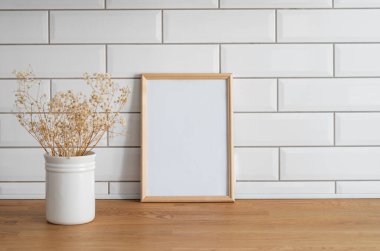Beyaz kiremit bir duvara karşı boş bir tuval ve kuru buketli tahta bir masanın üstünde duran hafif bir çerçeve. Fotoğraf, poster ya da resim tasarımı. Boşluğu kopyala.