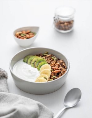 Beyaz bir masada muz ve kivi ile kaşık ve peçeteli granola. Sağlıklı kahvaltı konsepti vejetaryen yoğurt, fındık, müsli ve taze meyve.. 