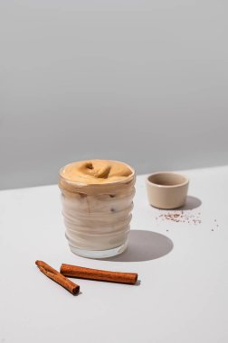 Dalgona kahvesi. Krem şantili buzlu kahve ve soya sütü. Gri arka planda tarçın çubukları ve gölgesi var. Moda ve popüler içki konsepti. 