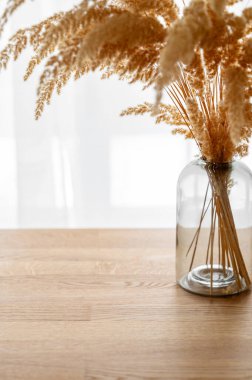 İskandinav tarzında bir pencerenin karşısındaki ahşap bir arka planda cam vazoda modern kuru otlar. Sanat deco konsepti, boho stili, yıldönümü hediyesi, doğum günü, anneler günü. Boşluğu kopyala.