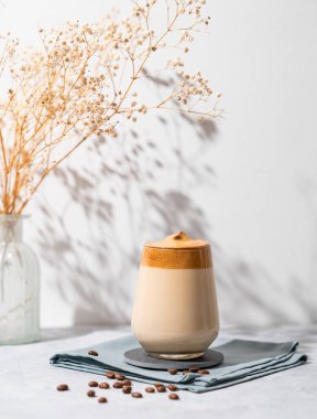 Dalgona kahvesi. Fasulyeli çırpılmış hazır kahve ve arka planda kuru buketli gölge. Moda ve popüler içki konsepti. 