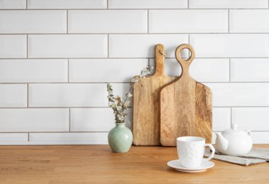 Tahta meşe masa üstü, bir fincan çay ve bir çaydanlık, kesme tahtaları ve kuru dalları olan bir vazo olan beyaz tuğladan bir arka plan. İskandinav tarzında samimi kahvaltı konsepti. Boşluğu kopyala.