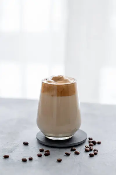 Whipped Dalgona coffee with milk. Instant  coffee in a glass with beans on a blue background with morning light. The concept of a trendy and popular breakfast drink.
