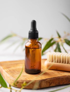 Ahşap bir tahtanın üzerinde, yeşil yapraklı gri arka planda fırçası olan bir şişeye çivi yağı ya da serum. Güzellik ve sağlık ürünlerinin sunumu, satışı veya reklamı için sahne ile kavram.
