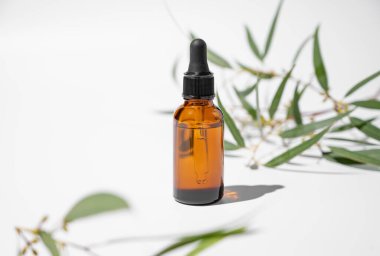 Beyaz arka planda yeşil yapraklı ve gölgeli bir şişede yüz ve vücut serumu. Sağlık ve güzellik ürünleri sunumu, satış veya kozmetik reklam afişi için sahne kavramı. Boşluğu kopyala.