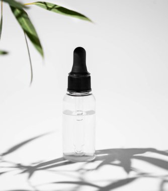 Beyaz arka planda yeşil yapraklı ve gölgeli vücut ve yüz masajı yağı. Sağlık ve güzellik ürünleri sunumu, satış veya kozmetik reklam pankartı konsepti. Ön görünüm.