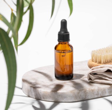 Yeşil yapraklı ve gölgeli beyaz bir arka planda fırçası olan mermer bir tahtanın üzerindeki bir şişedeki çivi yağı ya da serum. Güzellik ve sağlık ürünlerinin sunumu, satışı veya reklamı için sahne ile kavram.