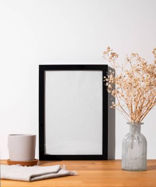 Açık bir duvara karşı boş bir tuval ve vazo ve fincanla ahşap bir masanın üstünde duran siyah bir çerçeve. Fotoğraf, poster ya da resim tasarımı. Boşluğu kopyala.