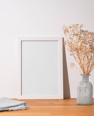 Beyaz bir çerçeve, beyaz bir çerçeve, beyaz bir duvar ve vazo ile ahşap bir masanın üzerinde. Fotoğraf, poster ya da resim tasarımı. Boşluğu kopyala.