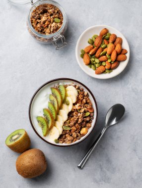 Mısır gevreği, yoğurt, muz ve kivi, arka planda hafif bir kasede. Doğal ev yapımı diyet kahvaltı konsepti süt ürünleri, fındık, granola ve taze meyveden yapılır. Üst görünüm.