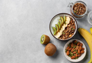 Mısır gevreği, yoğurt, muz ve kivi, arka planda hafif bir kasede. Doğal ev yapımı diyet kahvaltı konsepti süt ürünleri, fındık, granola ve taze meyveden yapılır. Üst görünüm ve kopyalama alanı.