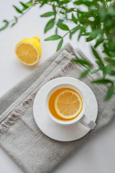 Beyaz bir masanın üzerinde limonlu, peçeteli ve yeşil dallı bir çay. Modern İskandinav tarzında iç mekan. Kahvaltı konsepti. Üst görünüm.