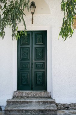 Sallanan okaliptüs dallarının altında beyaz duvarlı parlak yeşil kapısı olan eski bir ev. Kapalı kapı bir lambayla süslenmiş, eve rahat bir giriş sağlıyor. Korfu, Yunanistan.